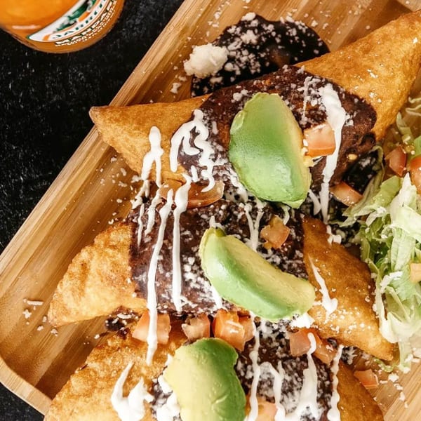 Three golden-fried El Jalapeño Bar & Grill empanadas topped with dark sauce, crema, avocado, and lettuce.