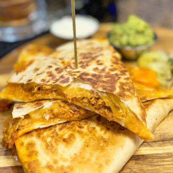 Chicken quesadillas with melted cheese, served with guacamole and sour cream on a wooden board.