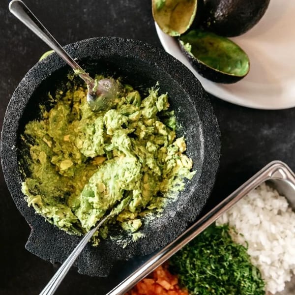 Freshly made guacamole in a molcajete with chopped onions, cilantro, and avocados nearby.